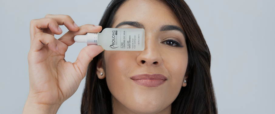 Woman holding Prolong Lash under eye serum bottle near her eye