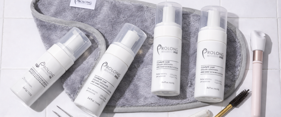 Flat lay of Prolong Lash cleanser bottles and tools on a white tiled surface with a grey towel.